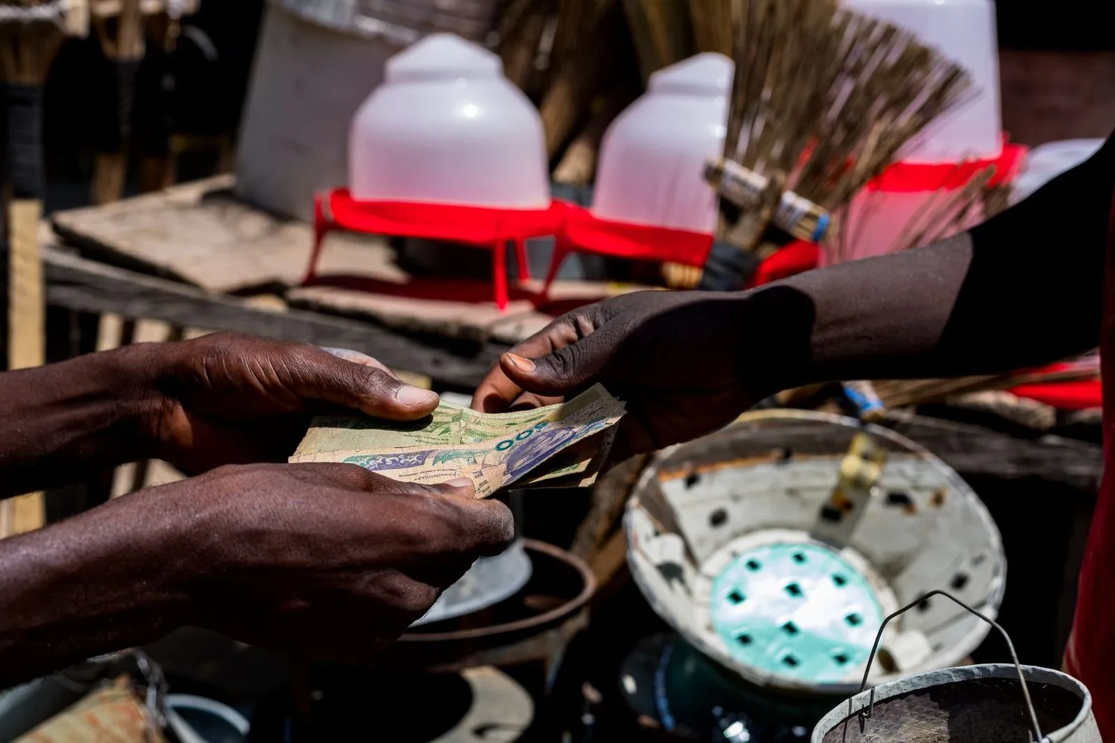 Stock photograph of hands exchanging banknotes at an outdoor market; the people and transaction shown are unaffiliated with Wanhoo