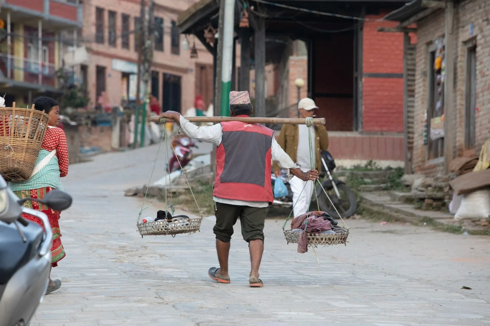 Stock photograph of a porter carrying goods on a street in Bhaktapur; the person and activity shown are unaffiliated with Wanhoo
