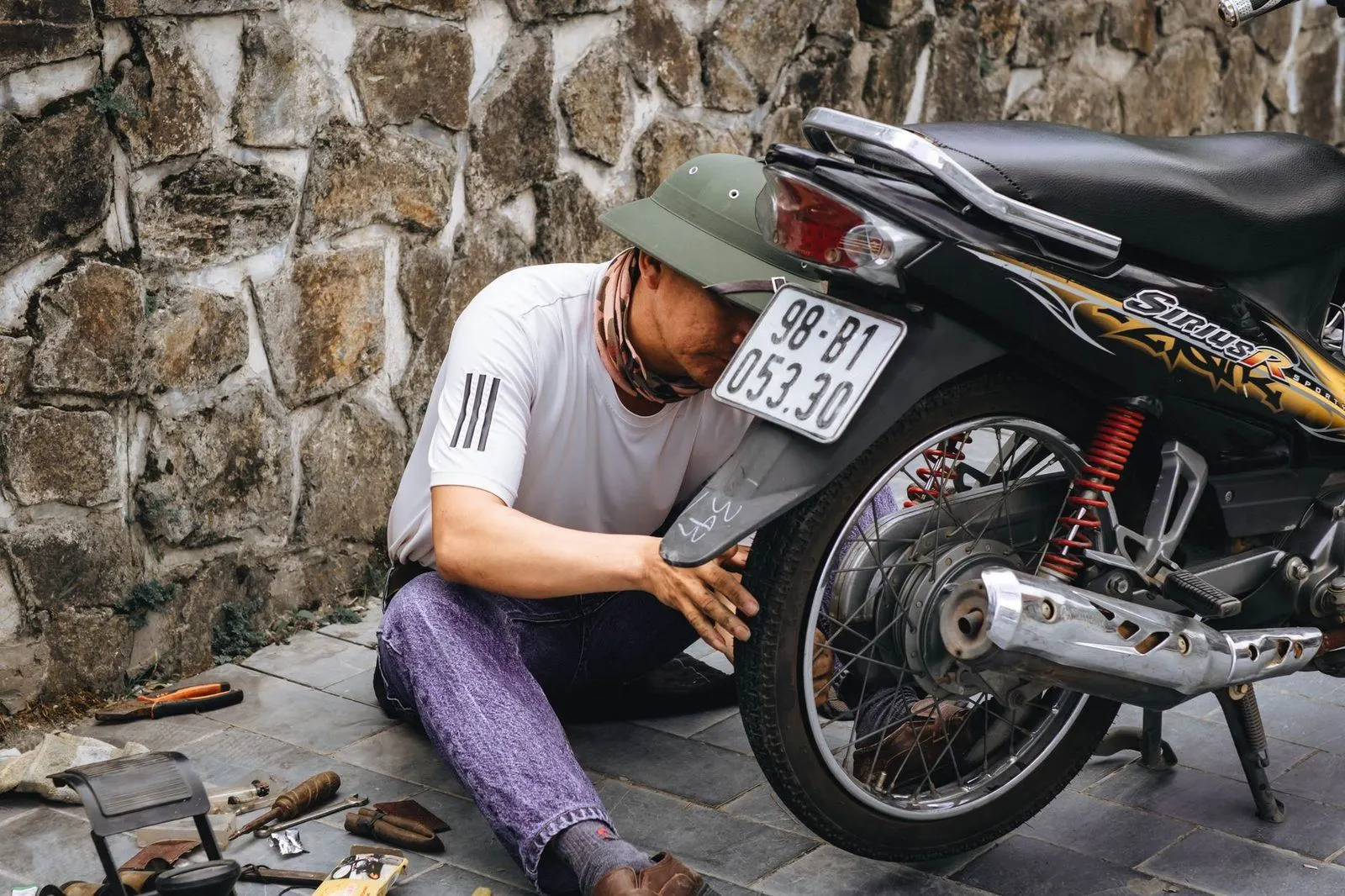 Stock photograph of a mechanic working on a motorcycle wheel outdoors; the person, workshop, and vehicle shown are unaffiliated with Wanhoo