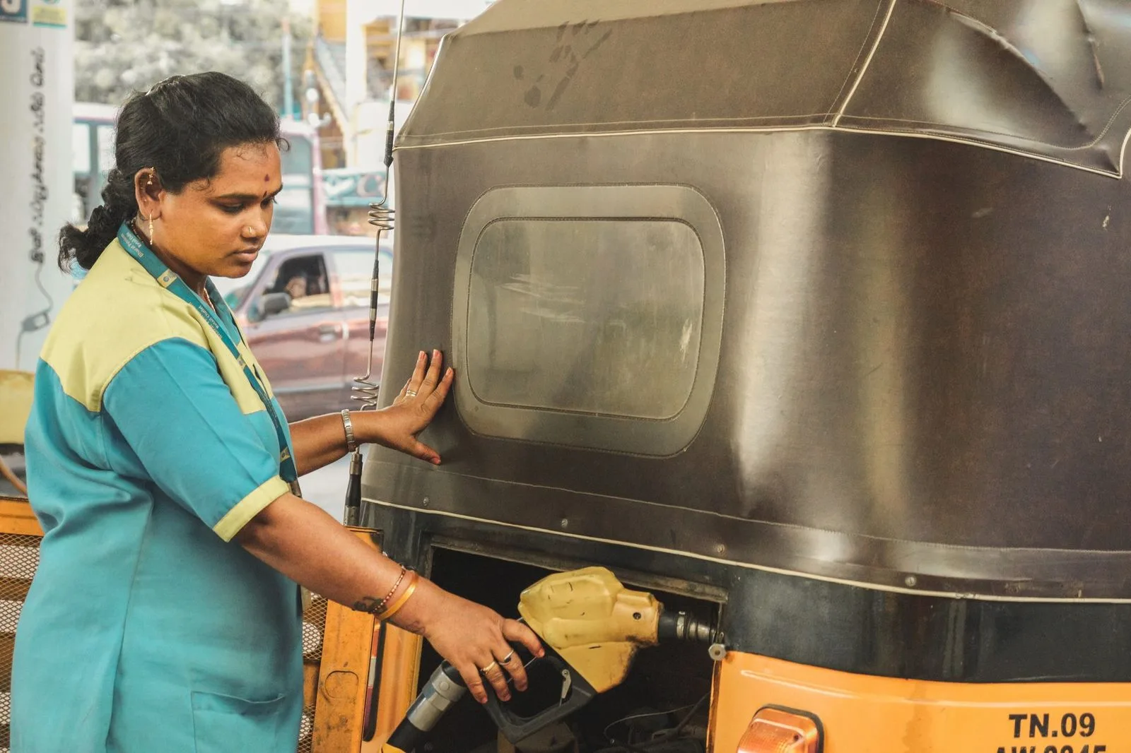 Stock photograph of a woman refuelling a three-wheeler at a roadside pump; the person and vehicle are unaffiliated with Wanhoo