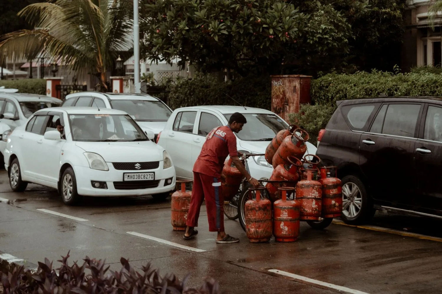 Stock photograph, unaffiliated with Wanhoo: a delivery worker moving gas cylinders through busy traffic in the rain