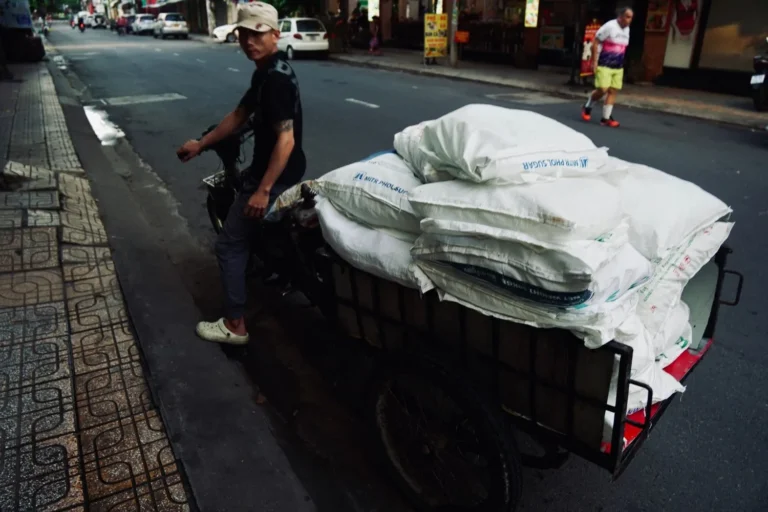 Stock photograph of a three-wheeled goods vehicle carrying sacks on a city street; unaffiliated with Wanhoo